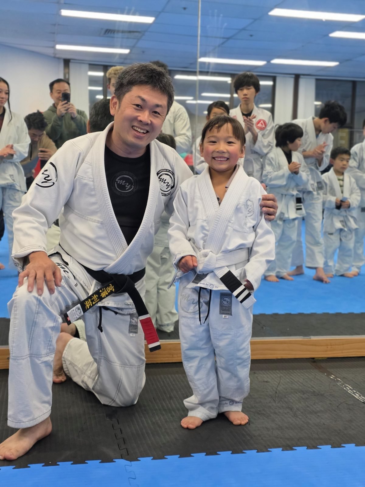 Toshi kneeling on the mat to tie a young child's belt